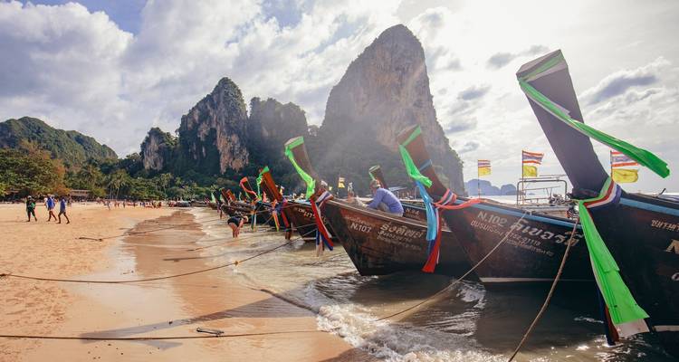 Des bateaux à longue queue ornés de rubans s'alignaient sur une plage dorée sous des falaises calcaires imposantes et un ciel lumineux.