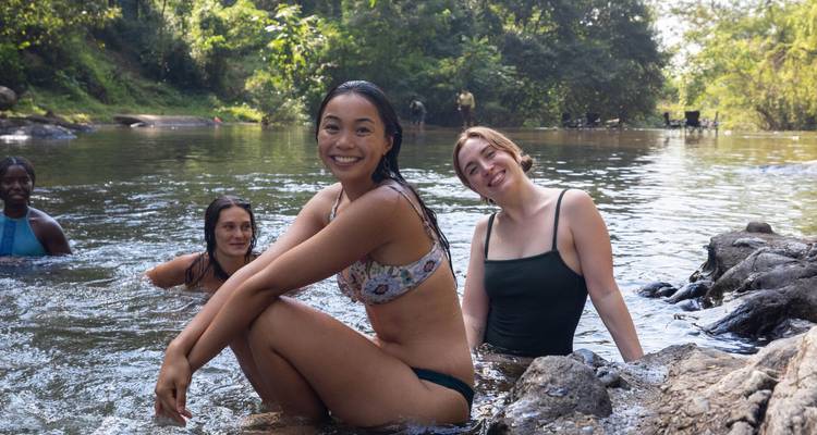Groupe de jeunes femmes riant et se détendant tout en se rafraîchissant dans un bassin de rivière en forêt.