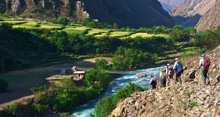 Gruppe von Menschen, die entlang eines Flusses in einem üppig grünen Tal wandern.
