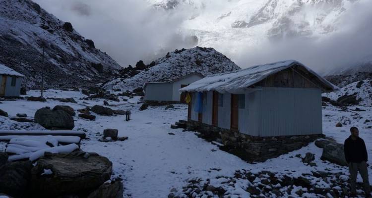 Schneebedeckte Hütten in einem Berggebiet mit bewölktem Himmel.
