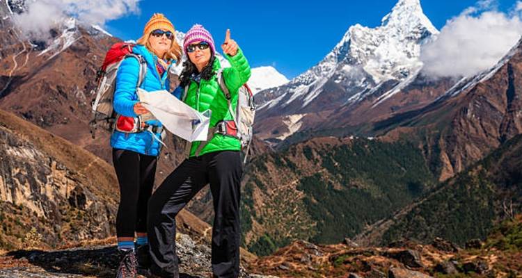 Zwei Wanderer mit Rucksäcken und einer Karte, die auf schneebedeckte Berge zeigen.