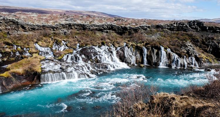 Rivière dévalant sur les rochers avec des montagnes enneigées.