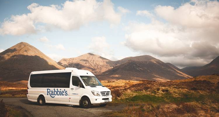 A 'Rabbie's' van in a scenic mountainous landscape.