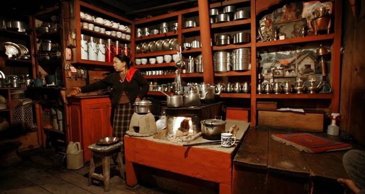 Inneres einer traditionellen Küche mit einer Frau und verschiedenen Kochutensilien.