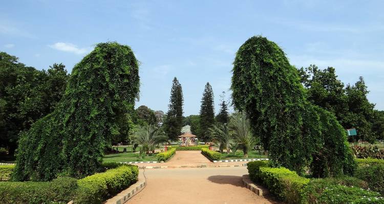 Tuin met gesnoeide heggen, paden en een open gebied dat leidt naar een structuur in de verte.