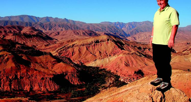 Persoon die op een heuvel staat met een uitgestrekt rood woestijnlandschap op de achtergrond.