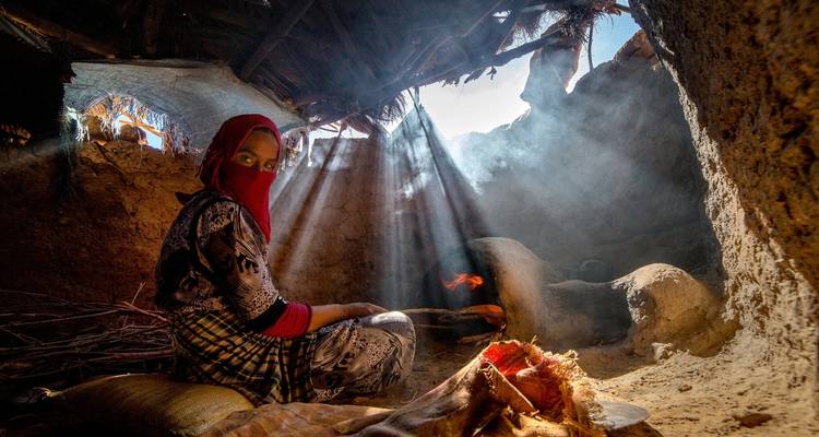 Persoon in traditionele kleding met zonlicht dat door dakkieren naar binnen stroomt.