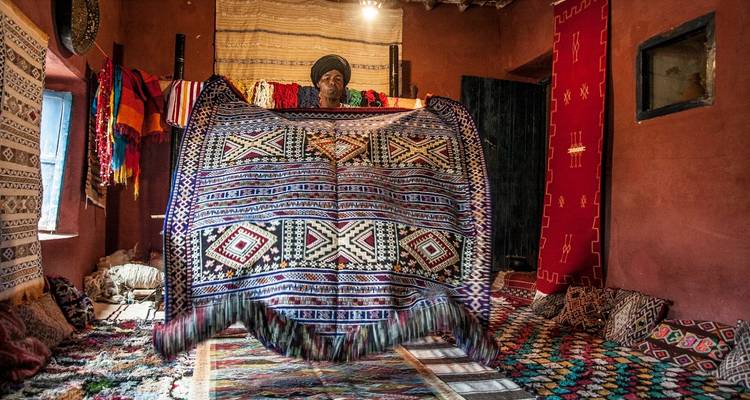 Een persoon die een groot traditioneel tapijt toont in een versierde kamer.