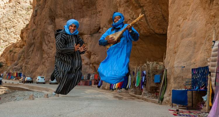 Twee mensen in traditionele kledij springen voor een rotsachtige kloof.