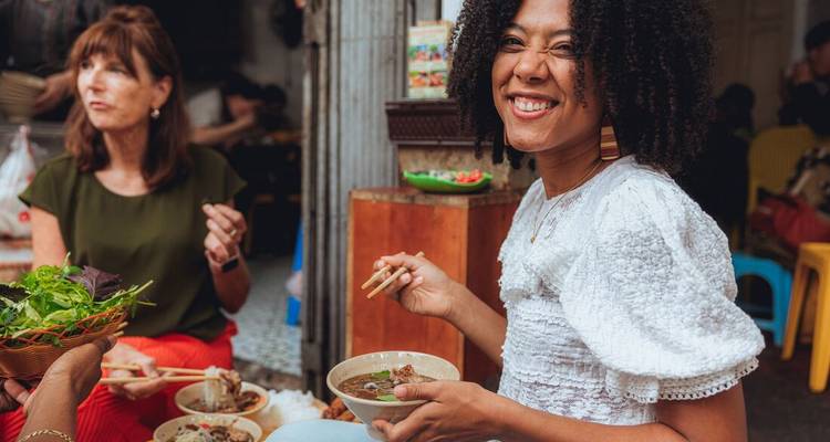 Un voyageur souriant savoure un bol de soupe de nouilles à un étal de rue vietnamien animé.