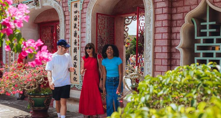 Trois voyageurs se promènent devant une porte de style chinois colorée ornée de calligraphie et de fleurs.