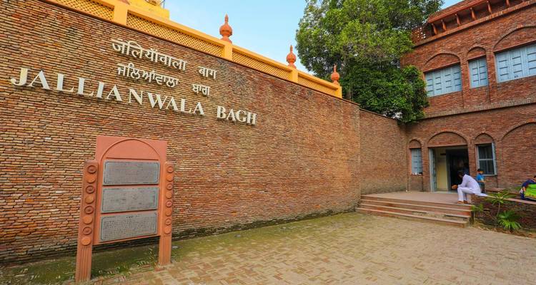 Ingang naar Jallianwala Bagh met bakstenen muur en bewegwijzering.