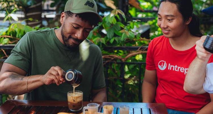 Dos hombres disfrutan del café vietnamita tradicional en una cafetería al aire libre rodeada de vegetación.