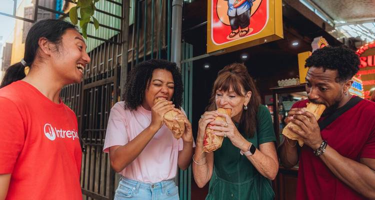 Unos amigos muerden entusiastas grandes sándwiches banh mi en un puesto callejero.