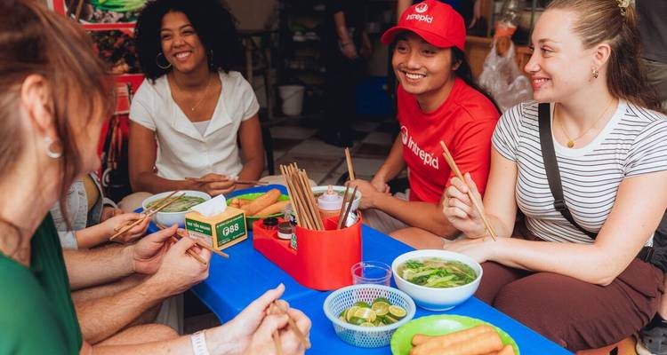 Los viajeros se sientan alrededor de una mesa azul baja disfrutando de humeantes tazones de pho vietnamita.