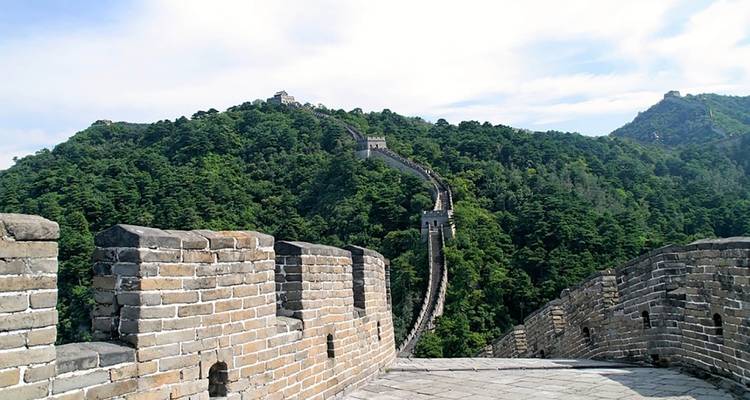 Section de la Grande Muraille de Chine serpentant sur des collines verdoyantes sous un ciel lumineux.