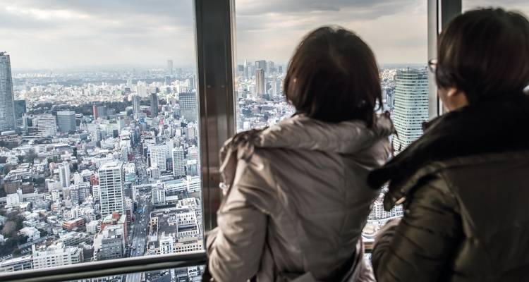 Deux visiteurs regardant l'horizon de Tokyo depuis une plateforme d'observation en hauteur.