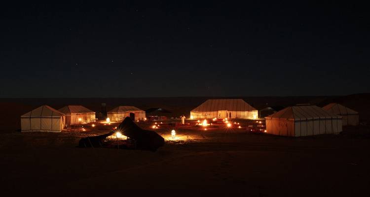 Nächtliche Szene von Wüstenzelten, die von Feuerschein unter einem sternenklaren Himmel beleuchtet werden.