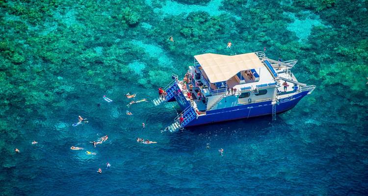 Aerial view of snorkelers around a catamaran above vibrant coral reefs in turquoise water.