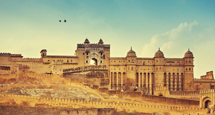 Panoramisch uitzicht op de zandstenen vestingwerken van Amber Fort tegen een warme avondhemel met twee vogels die zweven.