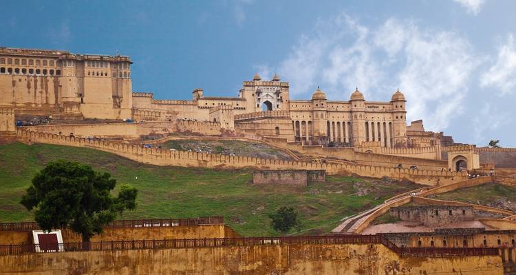 Amber Fort uitgestrekt langs een groene heuvel onder een blauwe lucht met verspreide wolken.