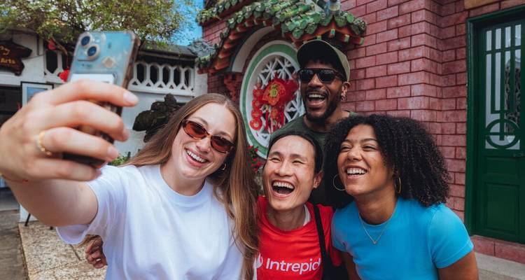 Quatre voyageurs joyeux se serrant les uns contre les autres pour un selfie devant un détail de temple circulaire coloré.
