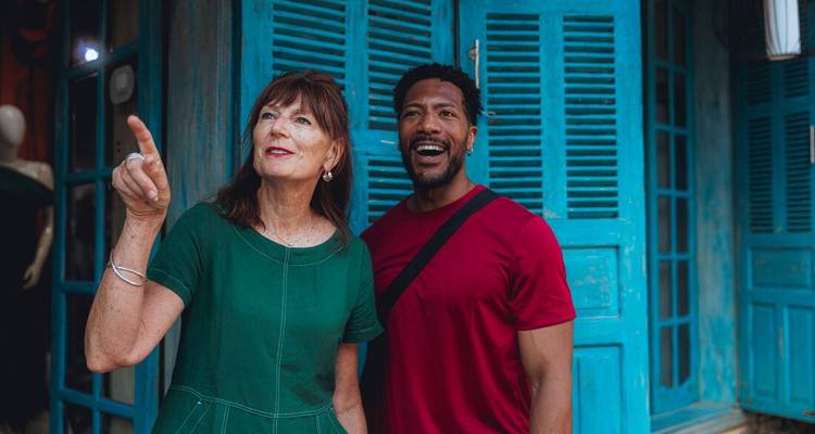 Duo souriant devant une devanture de magasin aux volets turquoise, la femme pointant du doigt quelque chose devant elle.