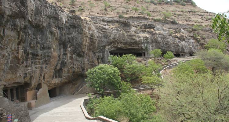 Rock-cut caves set against a rocky hillside with trees.