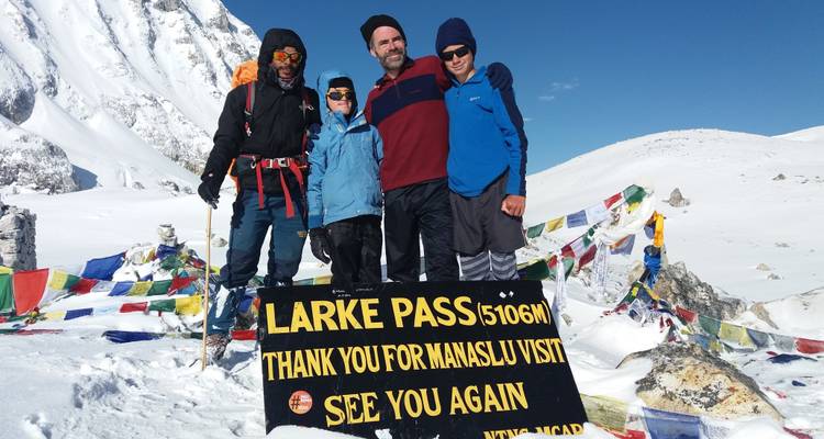 Vier Wanderer posieren mit einem Schild auf einem schneebedeckten Berggipfel.