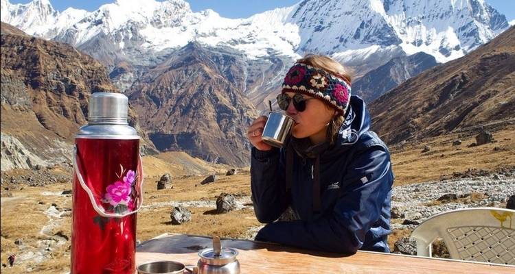 Persoon die uit een kopje nipt met bergen op de achtergrond.