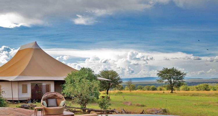 Luxuriöse Zeltlodge vor der Kulisse einer offenen Savanne unter bewölktem Himmel.