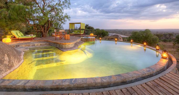 Atemberaubender Poolblick mit der Savanne und einem Sonnenuntergang im Hintergrund.