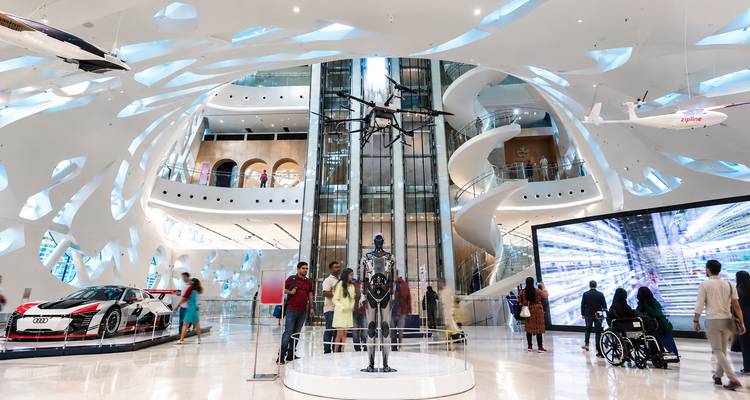 Futuristische interieur van een technologiemuseum in Dubai met spiraalvormige hellingen, drones en bezoekers die tentoonstellingen verkennen.