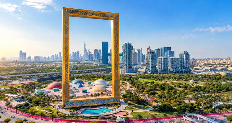 Luchtfoto van het gouden Dubai Frame dat uittorent boven een weelderig park met de skyline van de stad en de Burj Khalifa op de achtergrond.