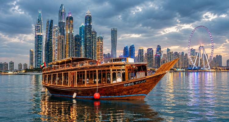 La traditionelle dhow en bois flotte sur des eaux calmes avec en arrière-plan l'impressionnante ligne d'horizon de la Marina de Dubaï au crépuscule.