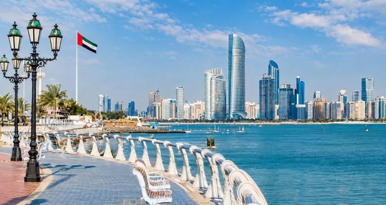 Skyline d'Abu Dhabi et promenade en bord de mer avec mât de drapeau émirati et eaux turquoise du golfe.
