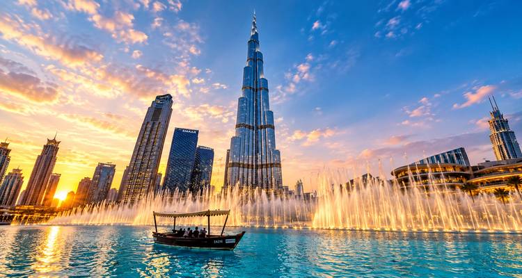 La Burj Khalifa se alza sobre el lago de la Fuente de Dubái en la hora dorada mientras los visitantes disfrutan de un paseo en un tradicional barco abra.