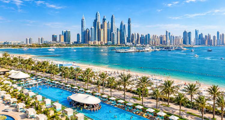 Piscina del resort y playa de arena blanca con la Palma Jumeirah y el skyline de Dubai elevándose al otro lado del golfo turquesa.