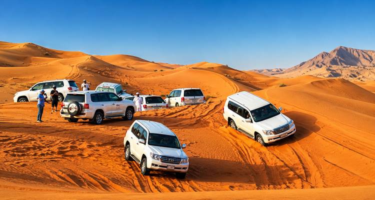 Convoi de véhicules tout-terrain blancs effectuant du franchissement de dunes sur les sables désertiques orange vif