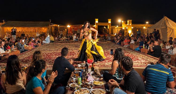 Camp désertique nocturne avec une danseuse orientale se produisant sur une scène recouverte de tapis devant les convives