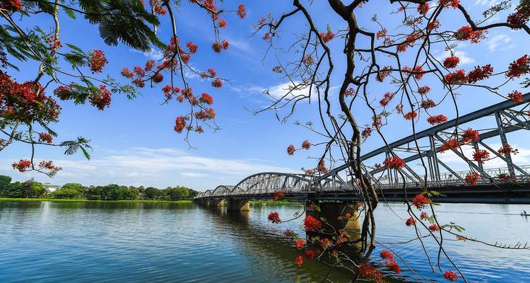 A bridge over a river with red flowers and blue sky.