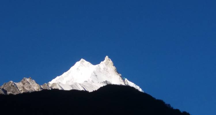 Besneeuwde bergtop onder een uitgestrekte blauwe hemel.