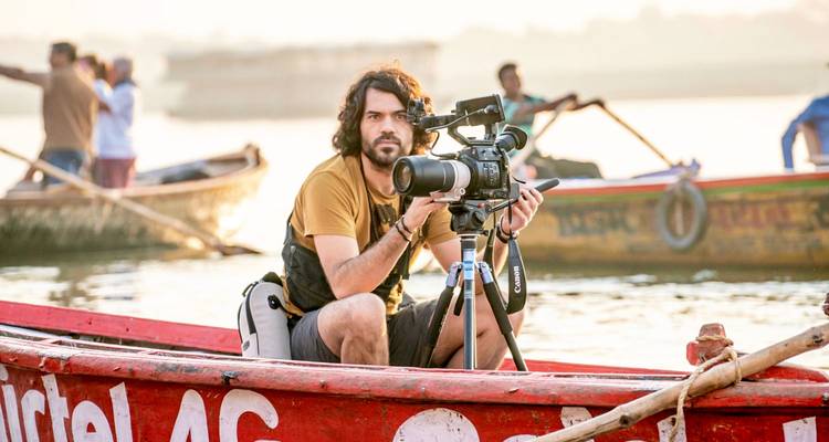 Una persona operando una cámara en un bote con otros remando.