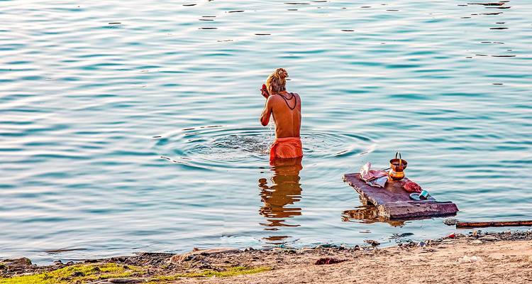 Una persona bañándose en un río, con pertenencias colocadas cerca.