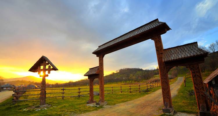 Portail en bois sculpté de Maramures et crucifix routier en silhouette baignés par un coucher de soleil éclatant