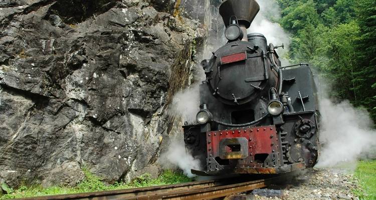Vue rapprochée d'une locomotive à vapeur noire émergeant d'un versant rocheux de montagne avec de la vapeur s'échappant en panache