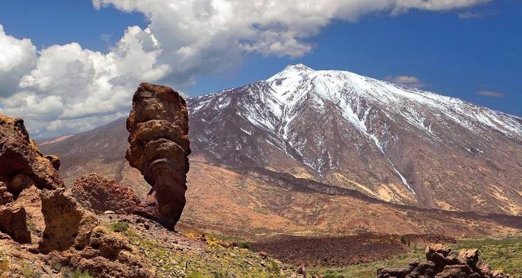 Snow-capped Mount Teide with rock formations in the foreground.