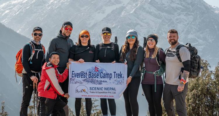 Gruppe von Wanderern mit Everest Base Camp Trek Banner und verschneiten Gipfeln im Hintergrund.