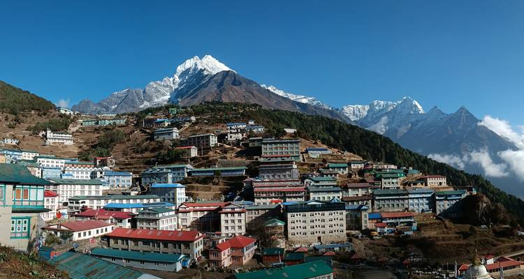 Panoramablick auf die terrassenförmig angeordneten Häuser des Namche Bazaar mit schneebedeckten Gipfeln, die sich majestätisch darüber erheben.