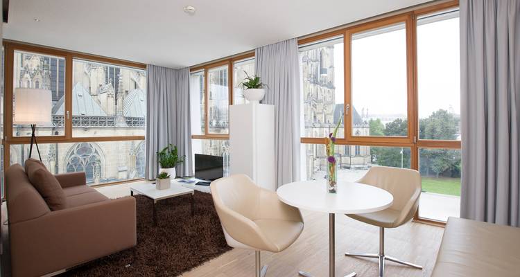 Suite d'hôtel spacieuse avec des fenêtres du sol au plafond donnant sur une cathédrale néo-gothique, mobilier moderne à l'intérieur.